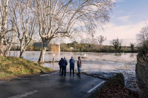 Residents look on as rising floodwaters cut off a local road, underscoring the need for stronger community preparedness.
