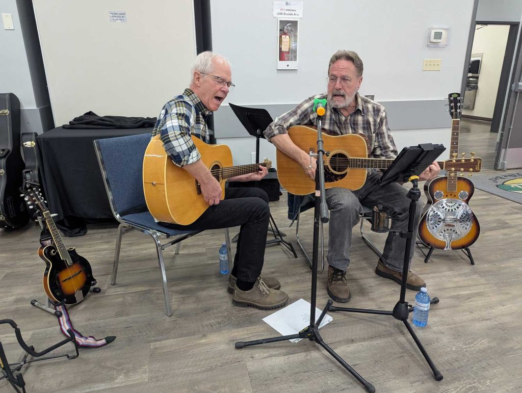 Live music fills the air at the Village of Lumby’s first Seniors Wellness and Food Fair. Two talented musicians entertain attendees with acoustic guitars and vocals at the White Valley Community Centre on October 21, 2025.